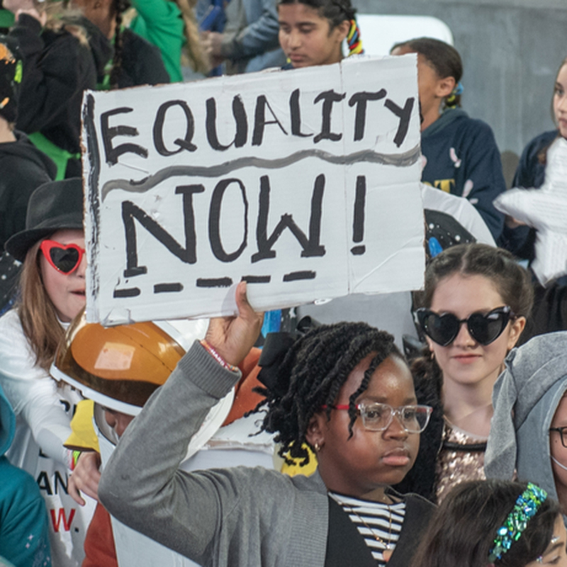 Student holding equality now sign.