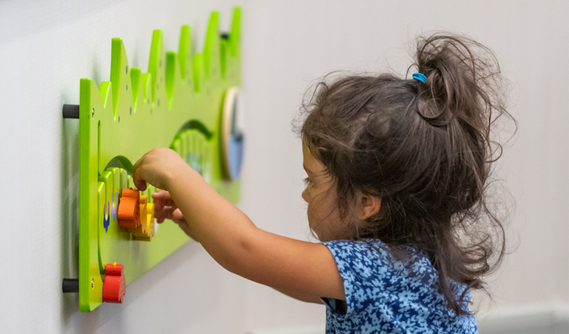 A small child playing with a sensory tool attached to the wall