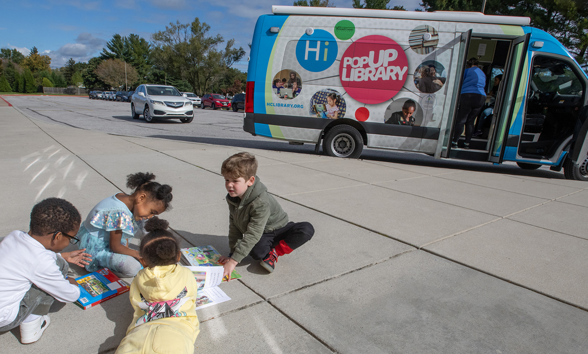 Children in a reading circle with the Library Bus in background.
