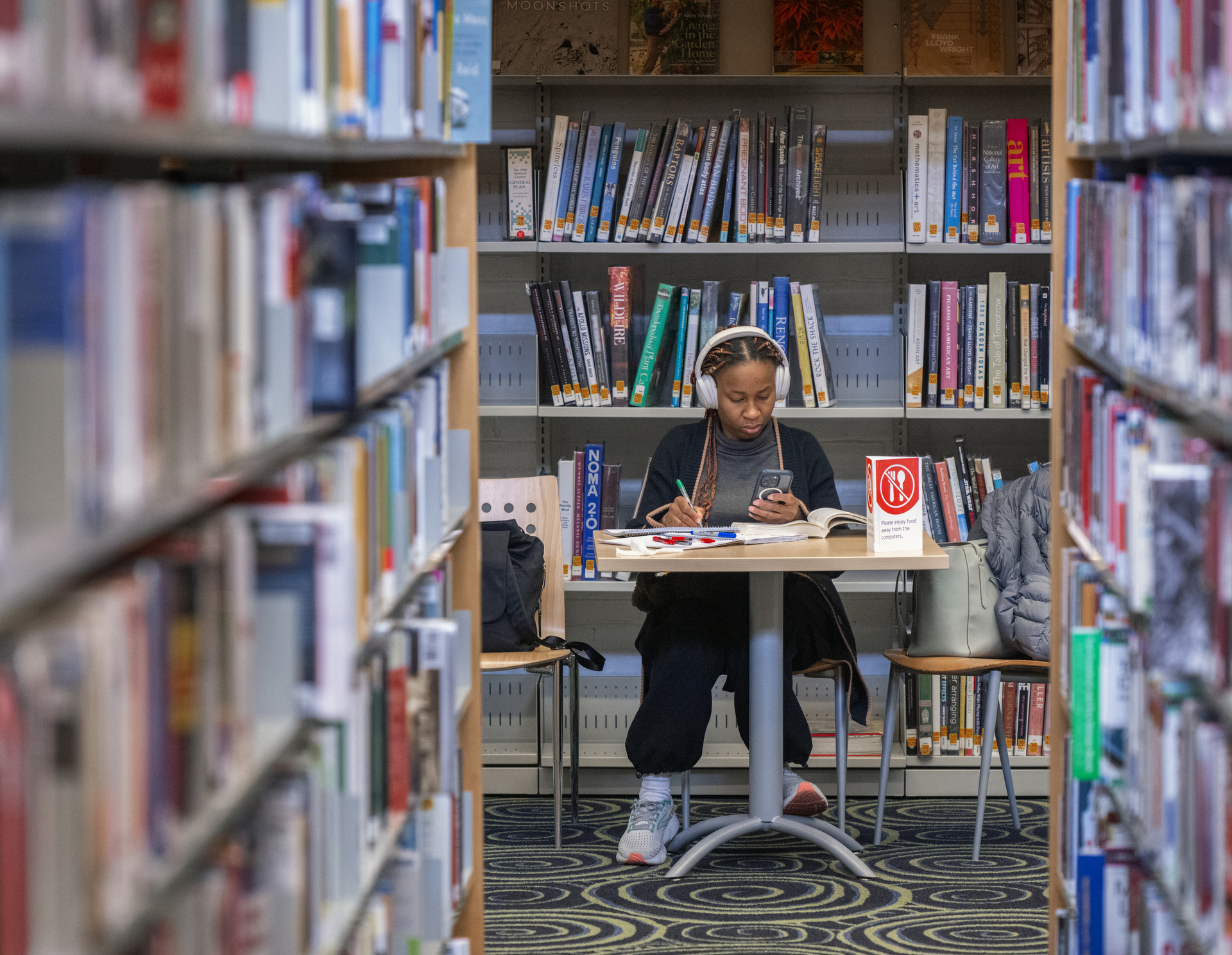 A student wearing earphones at a table covered in books.